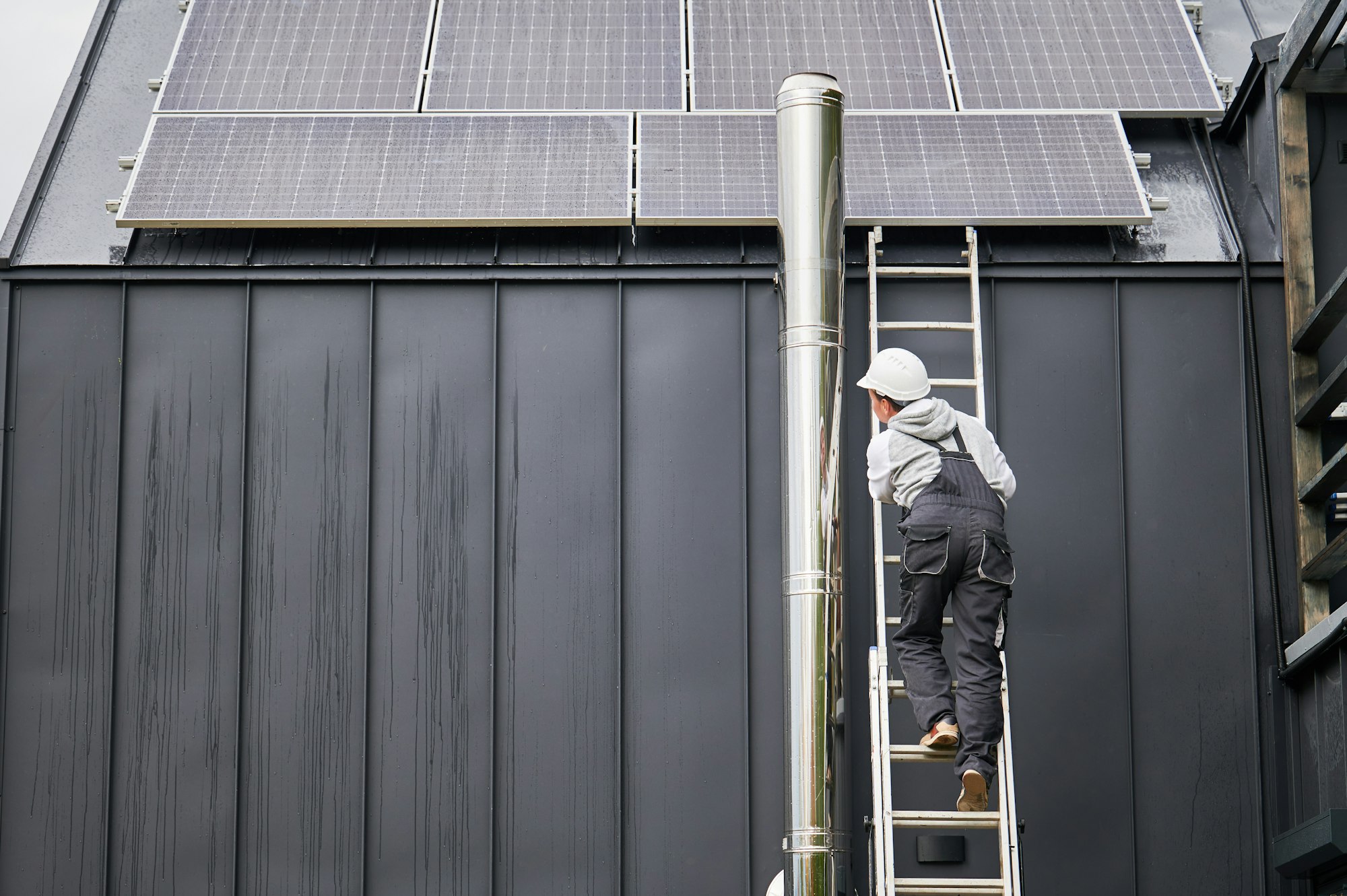 Technician climbing up the ladder while installing photovoltaic solar panels on roof of house.
