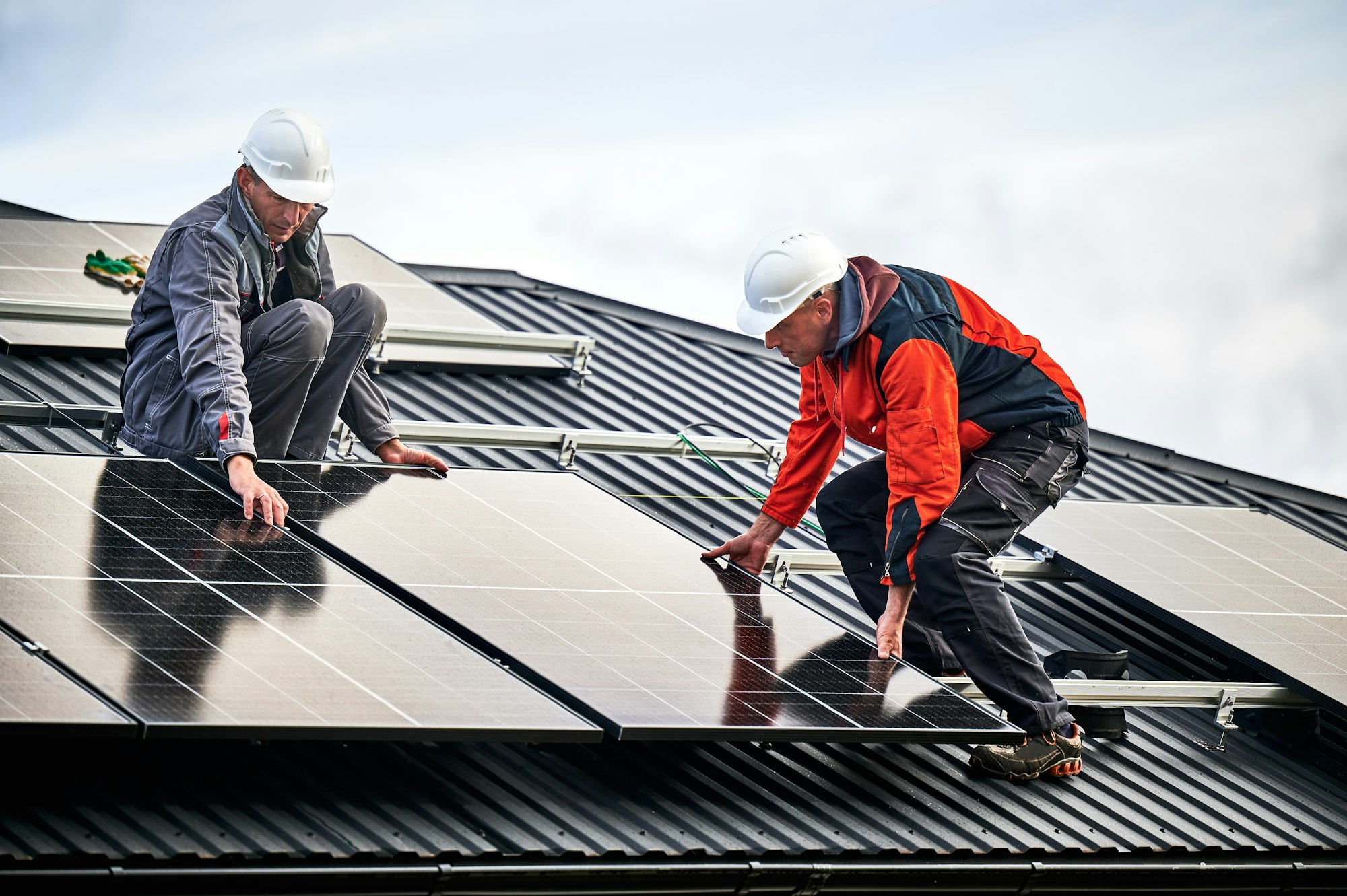 Men workers installing solar panels on roof of house.