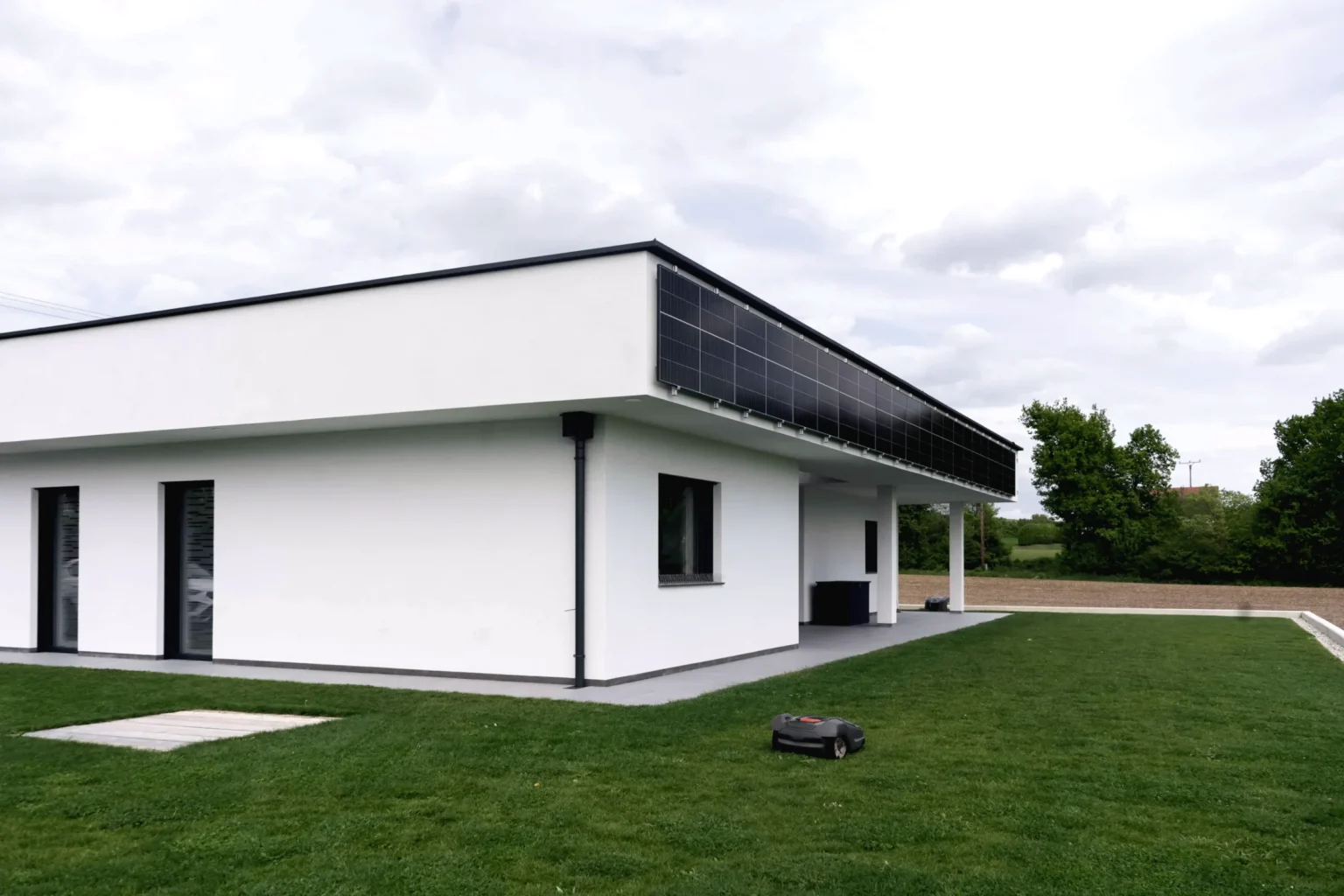 Einfamilienhaus mit Photovoltaik-Modulen an der Dachkante, Wiese im Vordergrund
